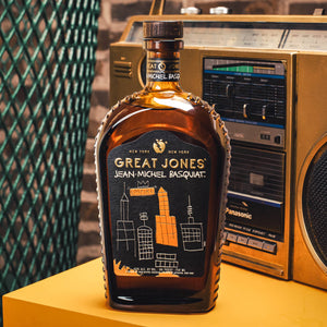 
                  
                    Great Jones x Jean-Michel Basquiat Empire Edition Straight Bourbon on yellow surface, placed in front of a brick wall and boombox
                  
                